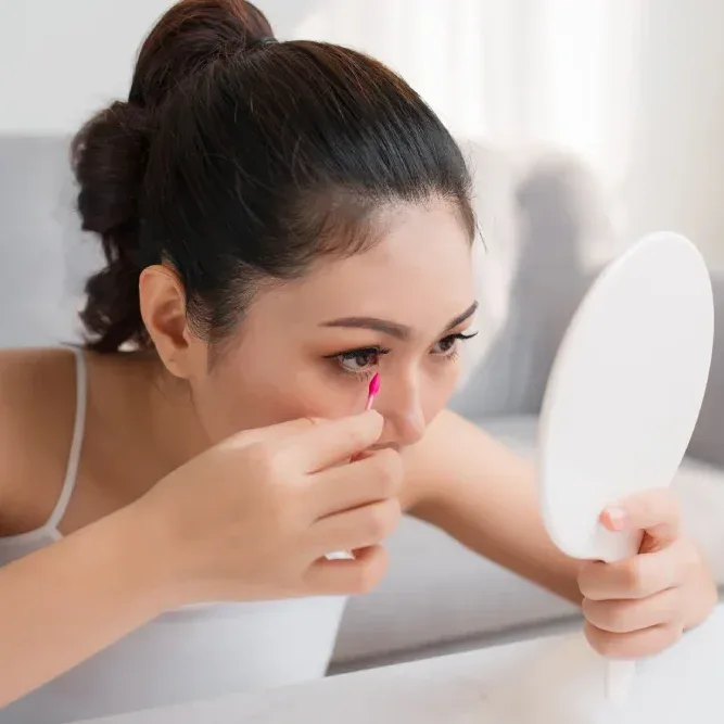 Woman applying dry eyeshadow with her finger while looking in a mirror.