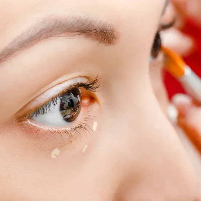 Woman applying oil-free foundation around her eye with a makeup brush.