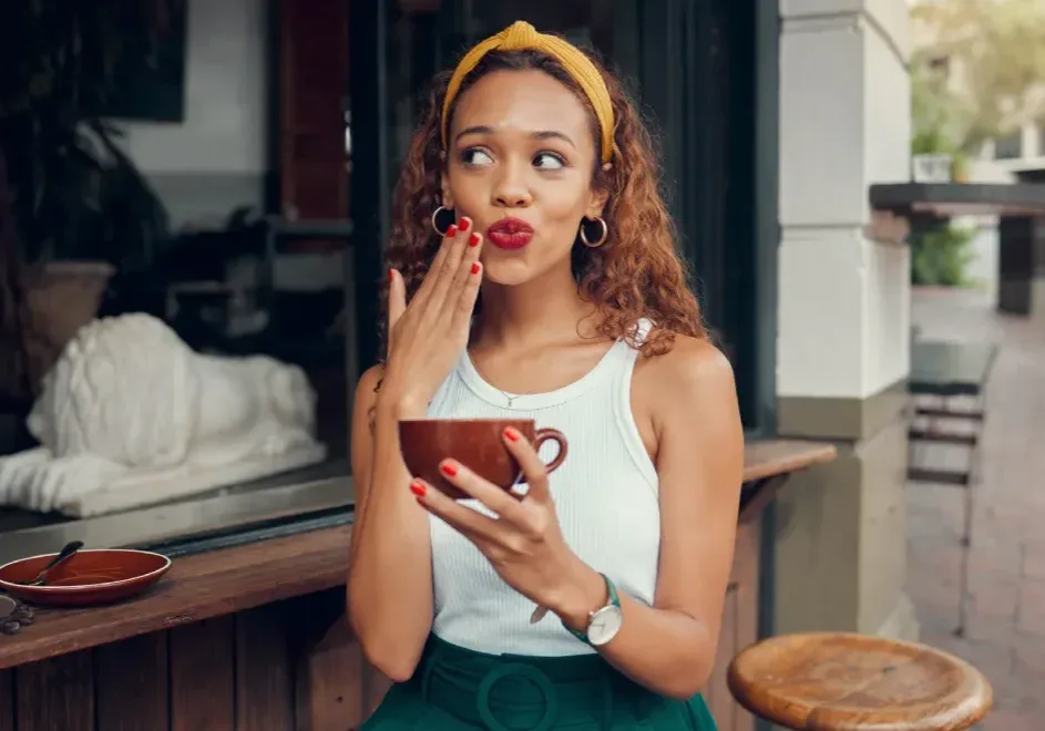 A woman with vibrant lipstick holds a coffee cup, illustrating the need to avoid drinks that can stain after a lip tattoo procedure.
