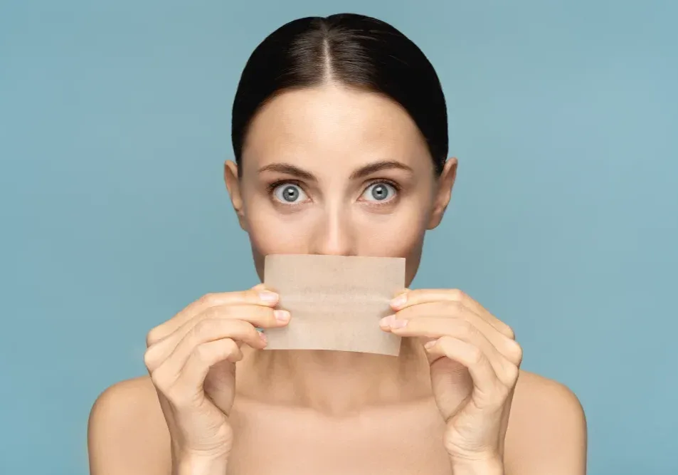 A woman demonstrates the correct technique for blotting lymph from her lips with a clean napkin after a cosmetic procedure to aid healing.