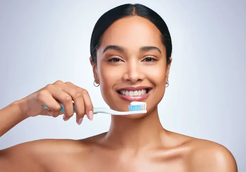 A smiling woman demonstrates how to gently brush teeth with a minimal amount of toothpaste to avoid ruining a new lip tattoo.