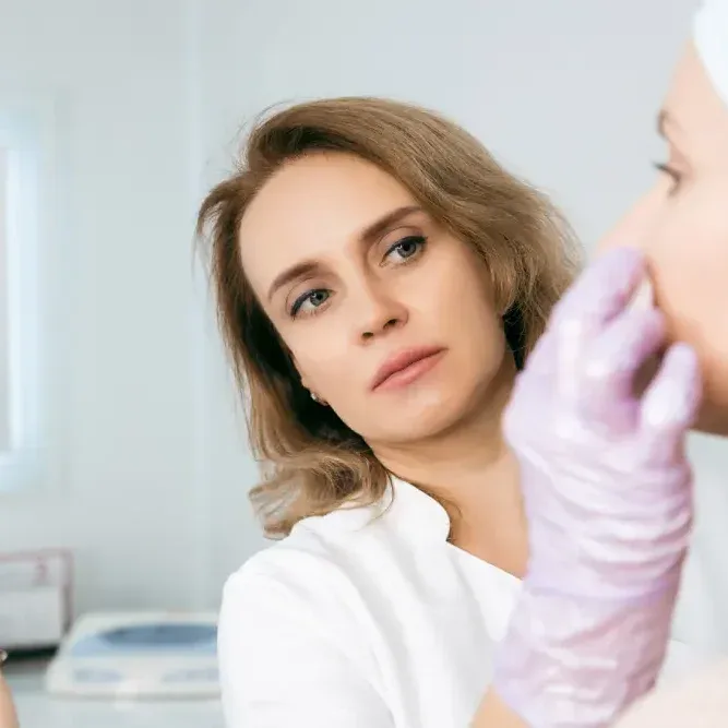 A client looks at her reflection while a dermatologist examines her skin.