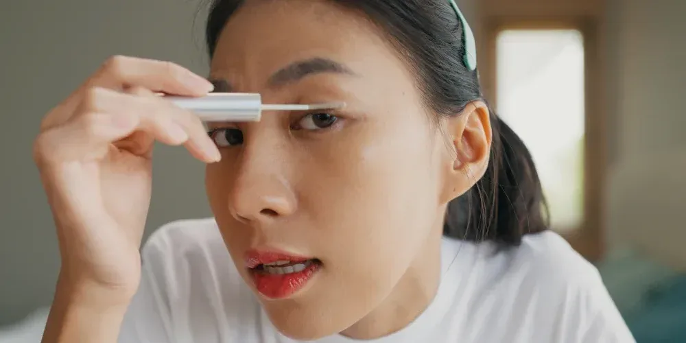 A woman carefully applies growth serum to her upper lash line, illustrating the method of how eyelash serums work.