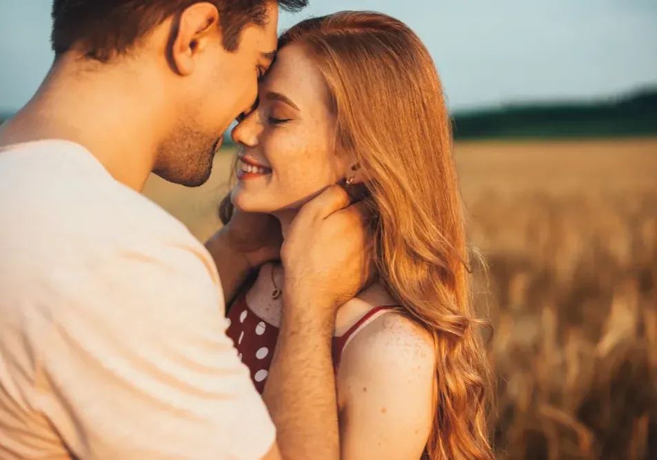 A happy couple embraces in a field, illustrating the desire to kiss, an activity to avoid for 7-10 days after a lip tattoo procedure.
