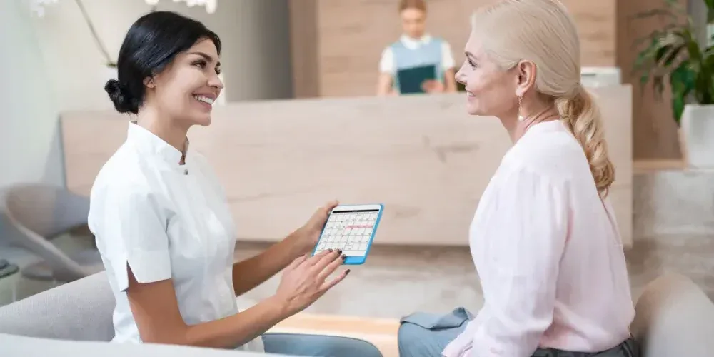 A lash technician reviews extension options with a client on a tablet.