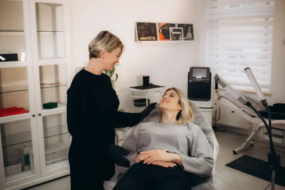 A lash technician consults with a client on the treatment bed, highlighting the key role of the consultation process.