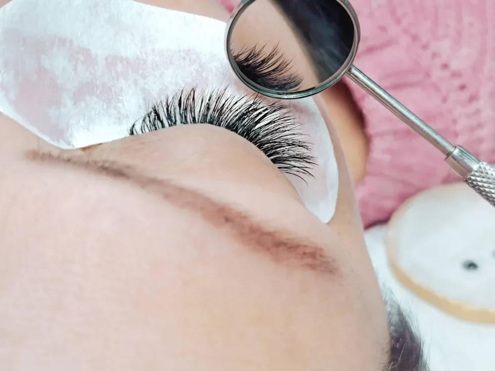 A technician uses a mirror to evaluate a client's natural lashes and eye shape.