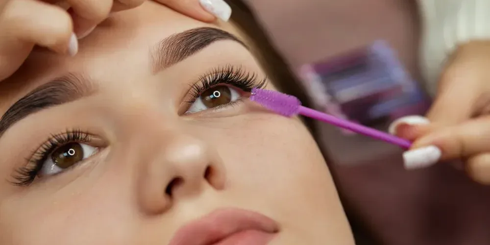 Close-up of a lash technician using a brush to groom eyelash extensions during a fill or maintenance appointment.