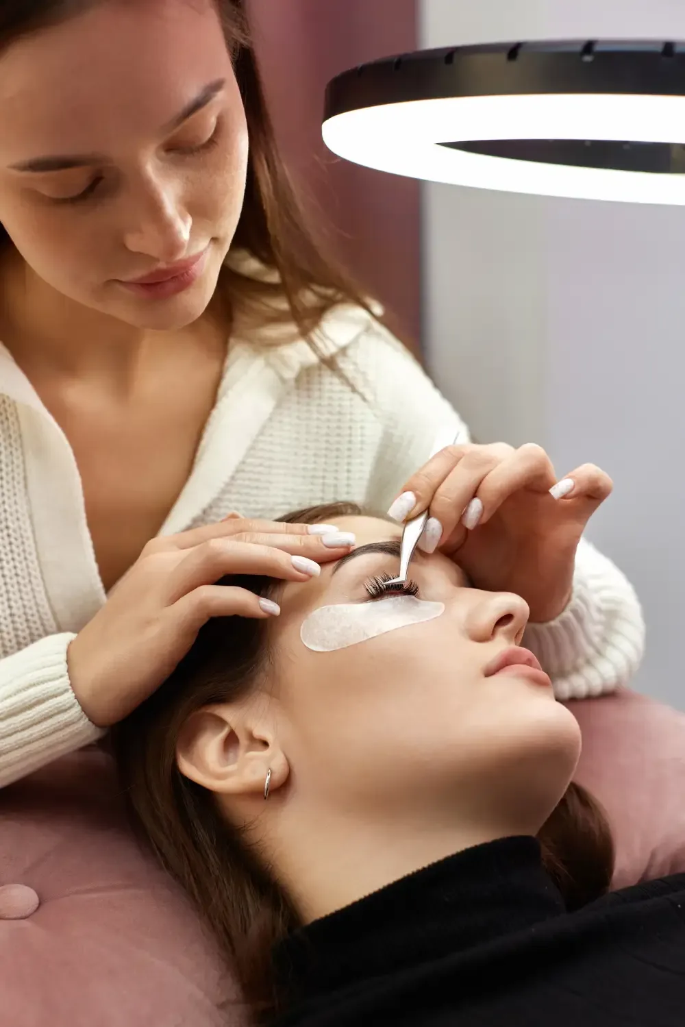 A technician applies protective under-eye patches to isolate the lower lashes before the removal process.