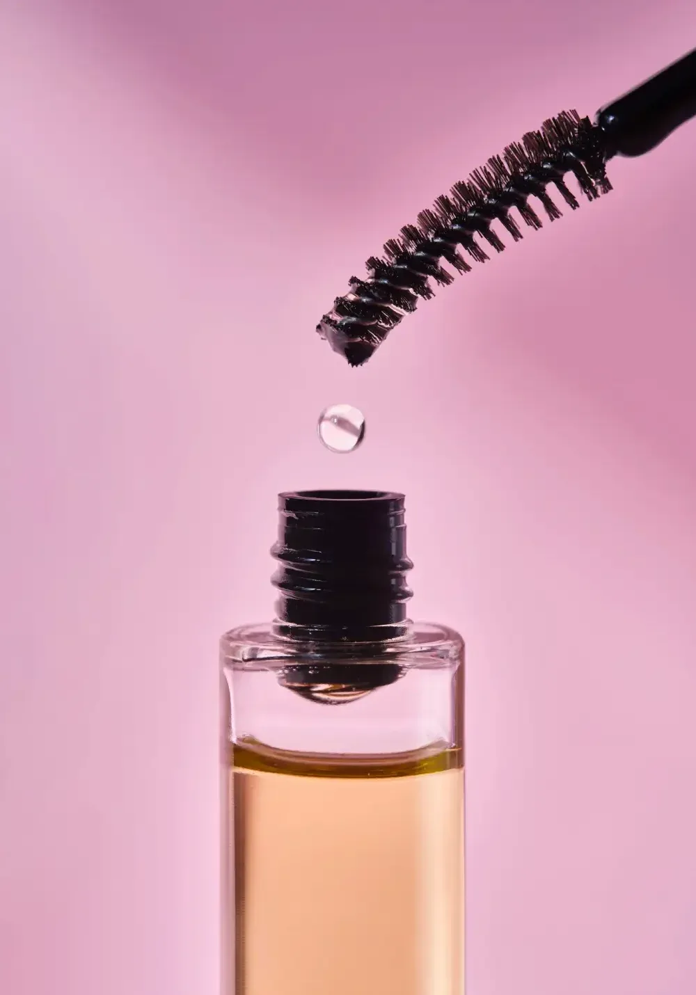 A drop of liquid on an applicator wand over a bottle, representing the key ingredients found inside eyelash serums.