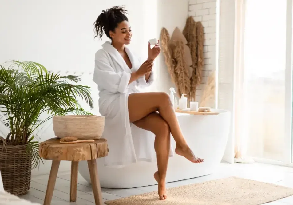 A woman in a bathrobe considers a natural balm, illustrating the use of approved alternatives like grapeseed oil for lip blush aftercare.