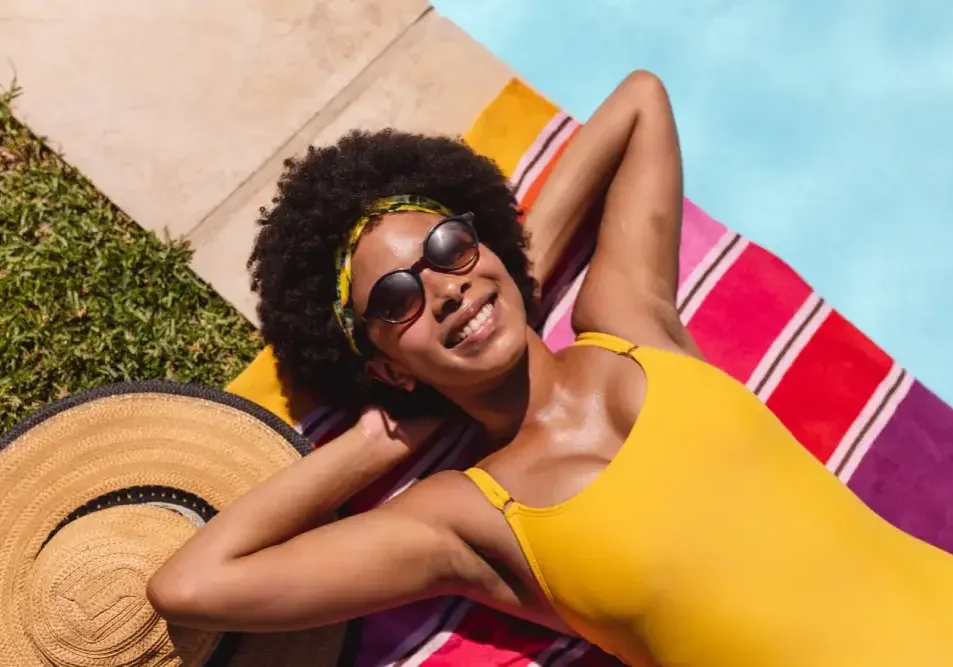 A smiling woman sunbathing by a pool, illustrating the critical need to avoid sun exposure to prevent hyperpigmentation during lip neutralization healing.