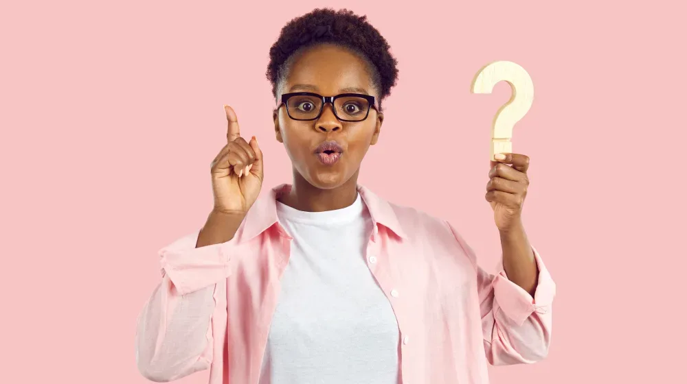 A woman with glasses holds a question mark, representing a client asking frequently asked questions about the cost of lip tattooing.