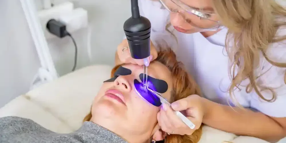 A lash technician uses a modern UV light curing system on a client, demonstrating a professional eyelash extension procedure.