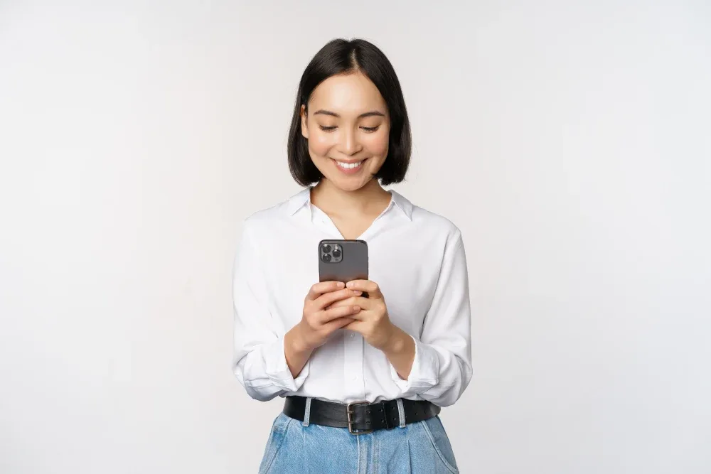 A smiling woman reads online reviews on her smartphone to find a reputable lash salon and technician.