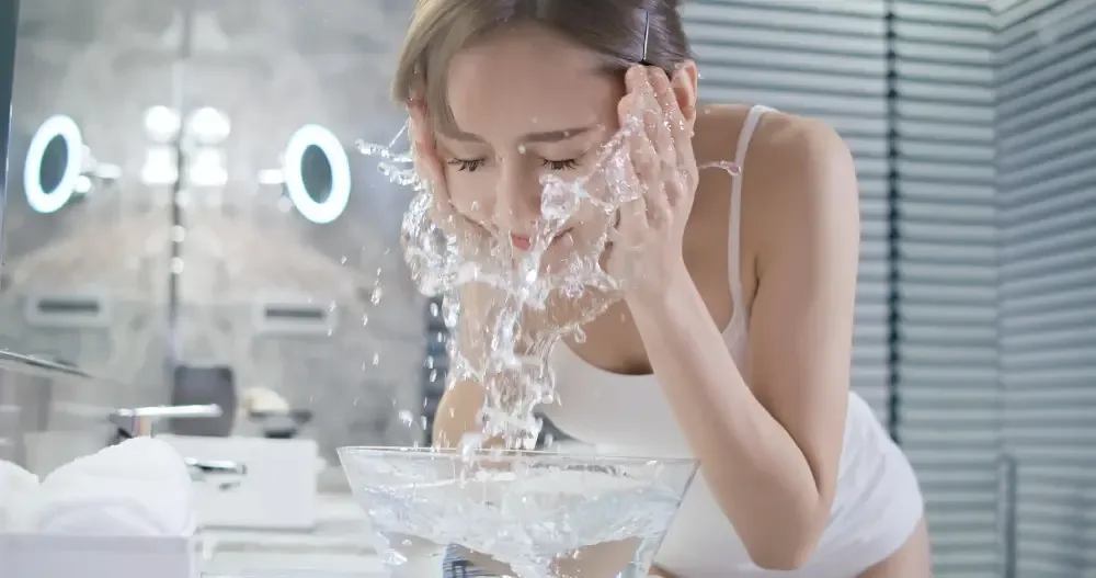 Woman washing her face with water while wearing eyelash extensions.