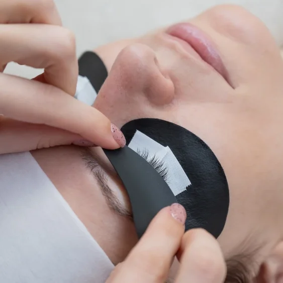 Beautician positions UV/LED curing lamp near client's protected eyes during extension bonding