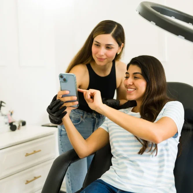 A client shows her phone to a technician during consultation, illustrating the importance of assessing communication skills and professionalism.