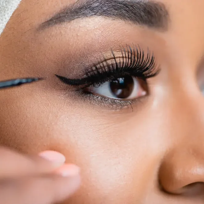 A close-up of an eye as eyeliner is carefully applied above the lash line with short, controlled strokes.