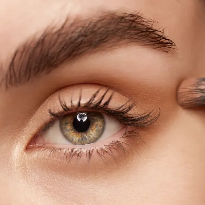 A soft brush applies eyeshadow with light, patting motions around the eye area, avoiding the lash line.
