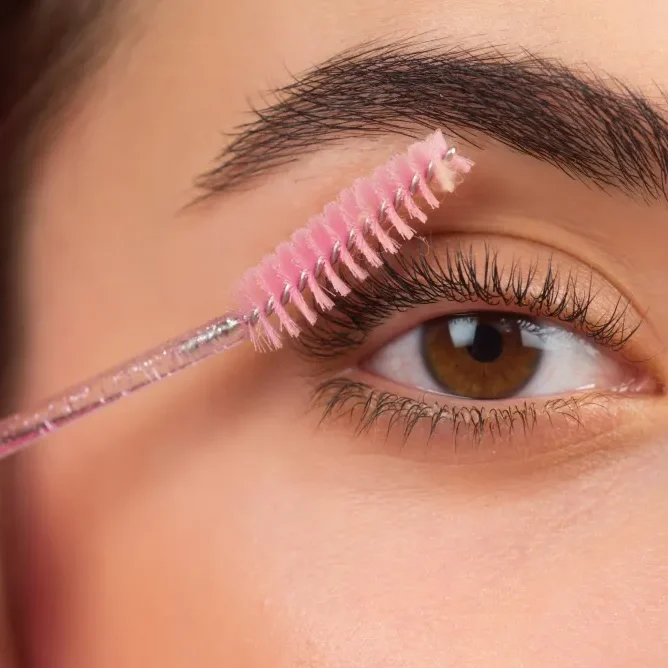 A spoolie gently grooms eyelash extensions, demonstrating the "gentle touch" rule to minimize friction and avoid damage when handling makeup.