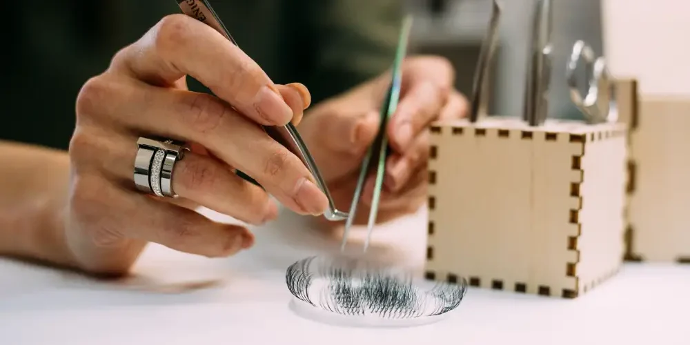 Cost: Professional Extensions vs. Home Kits A lash artist's hands skillfully create a volume fan with tweezers, representing the professional service included in the salon cost.