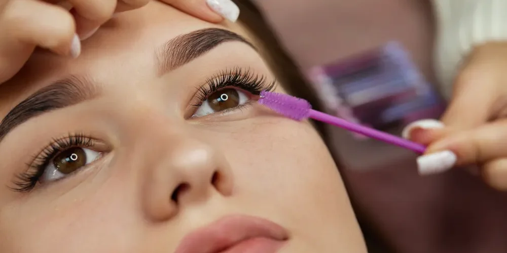 Eyelash Extension Fill Procedure Close-up of a lash technician using a brush to groom eyelash extensions during a fill or maintenance appointment.