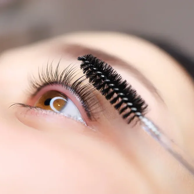 A spoolie brushes curled natural lashes, showing the bending effect from the chemical modification process of eyelash lamination.