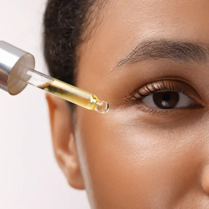 A woman applies an oil-based serum with a dropper, illustrating the rule to avoid oils to protect eyelash extension glue.