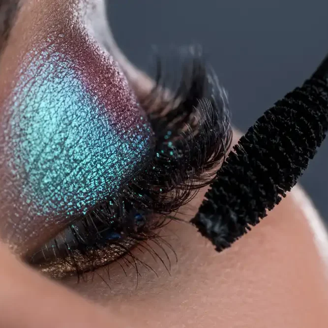 A mascara wand is applied to dramatic eyelash extensions, illustrating the caution against using waterproof makeup formulas.
