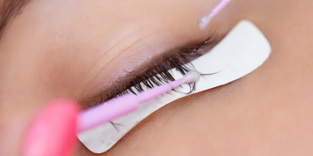 Professional Lash Extension Removal Close-up of a technician using micro-brushes to apply a remover product for a safe, professional lash removal.