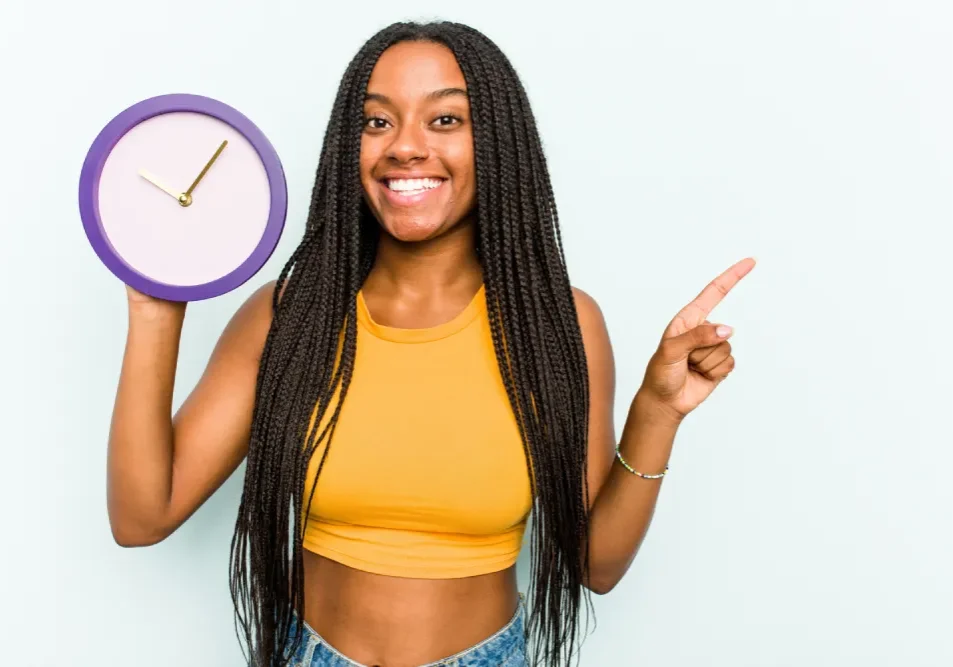 A smiling woman holds a clock, illustrating that lip tattoo results fade gradually over 1.5 to 3 years and require periodic updates.