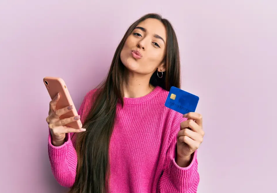 A woman holds a credit card and phone, representing the financial investment required for high-quality lip tattooing and future corrections.