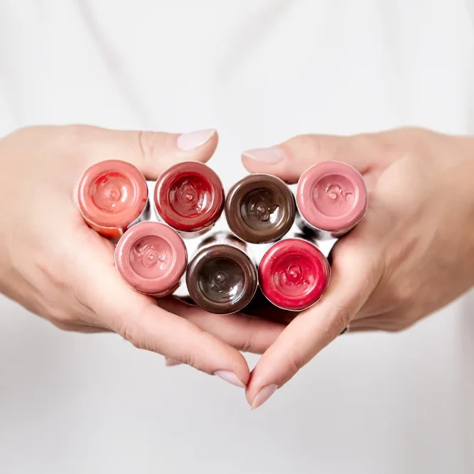 Hands hold a collection of pigment bottles, representing the artist's choice of materials and knowledge of color theory and coloristics.