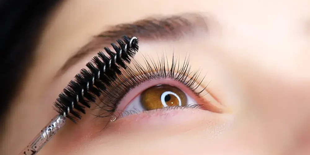 A spoolie brush grooms beautifully lifted natural lashes, showing the result of an eyelash lamination or lash lift procedure.