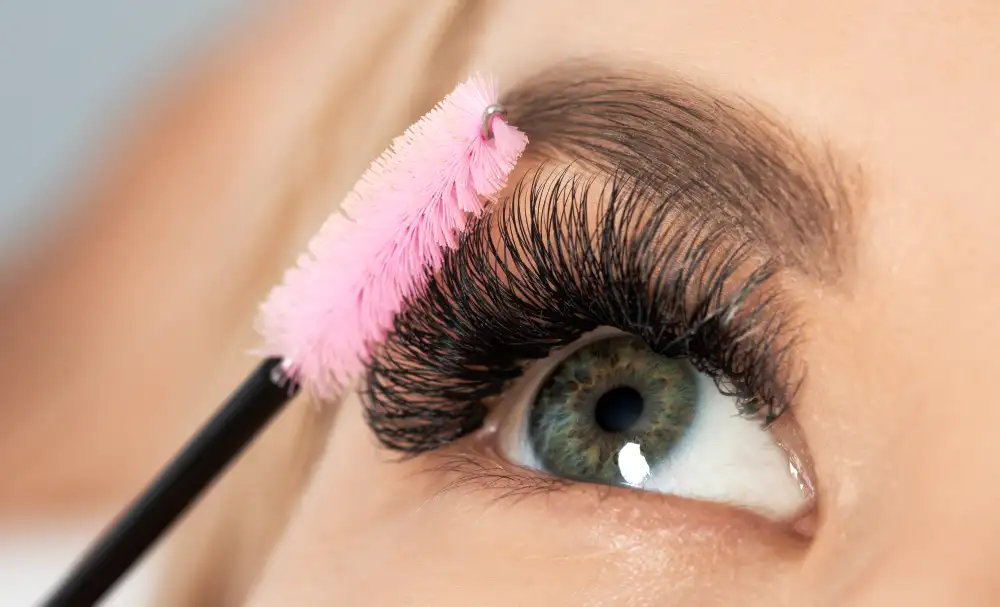 Beautician grooms finished UV/LED eyelash extensions with pink brush showing dramatic volume results