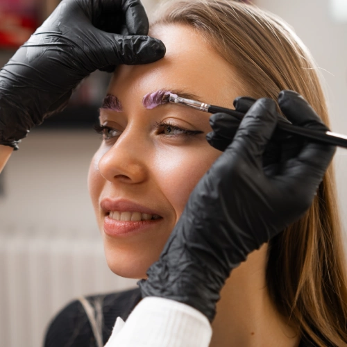 Master in black gloves applies formula to eyebrows using clinical sanitation protocols.