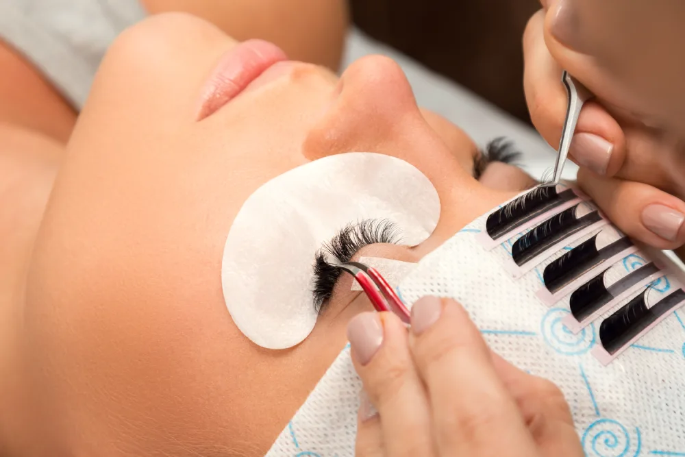 A technician carefully attaches artificial fibers to a client's natural lashes, demonstrating the process of eyelash extensions.