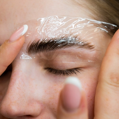 Close-up of eyebrow lamination process with plastic wrap covering brow hairs for setting.
