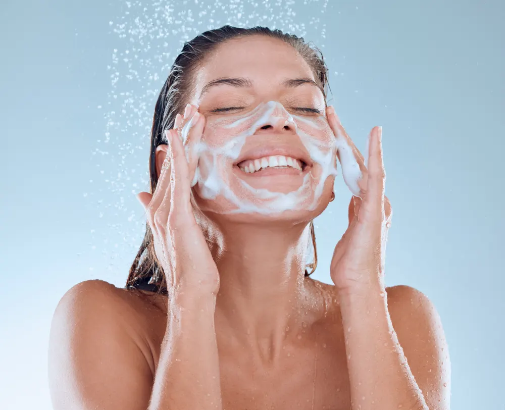 A woman happily washes her face with a foaming cleanser, following the initial aftercare instructions provided by her lash technician.