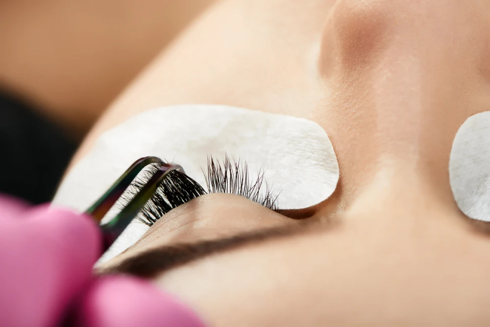 Close-up of a lash technician applying new eyelash extensions to natural lashes where old extensions were removed.