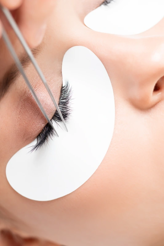 A macro shot showing the precise, professional technique of applying a lash extension fan to a single isolated natural lash.