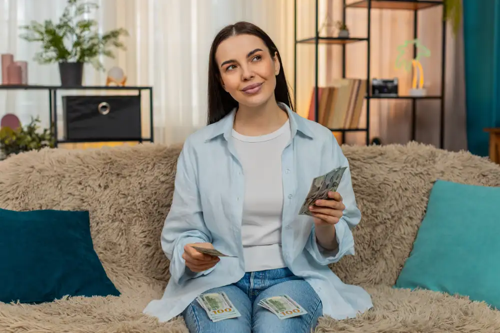 Budgeting for Eyelash Extension Maintenance A woman holding cash sits on a couch, planning her budget for eyelash extension maintenance and fills.