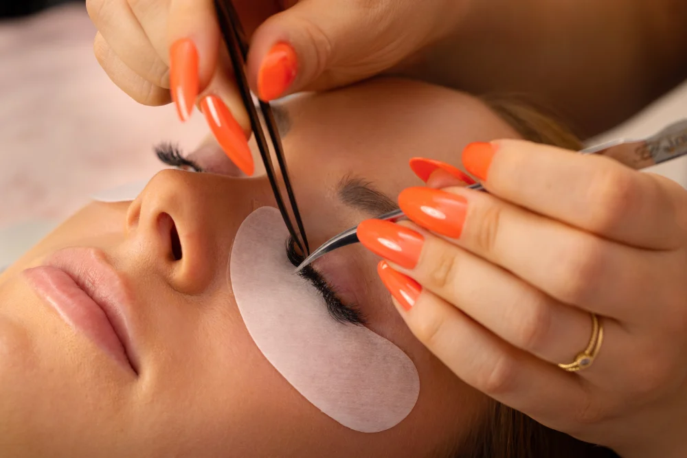 A technician carefully applies an eyelash extension with tweezers, demonstrating the professional use of high-quality lash glue.