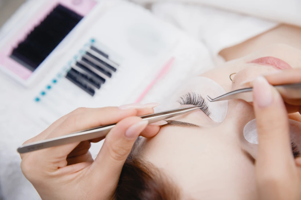 A technician dips a lash into a drop of adhesive, showing the quality materials that influence the final price.
