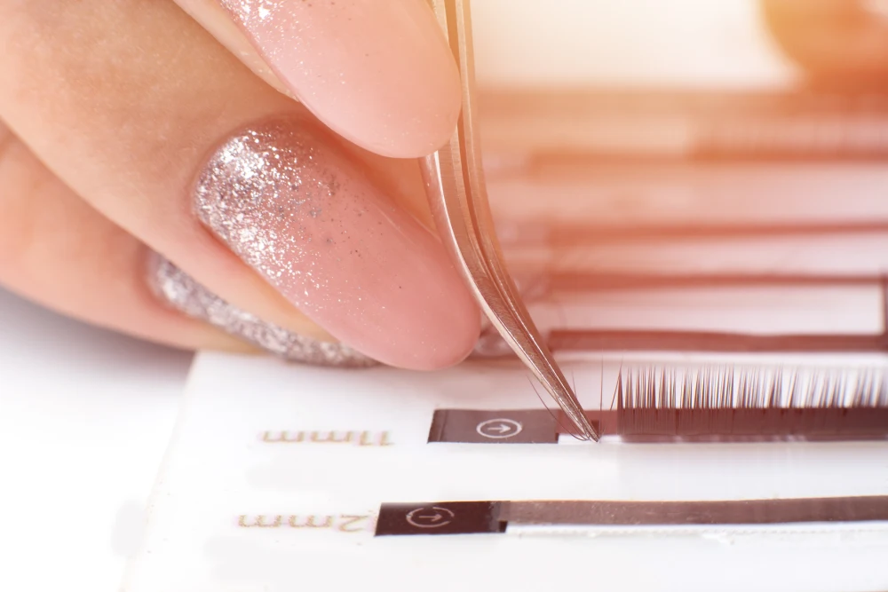 A technician uses tweezers to select a lash, representing the quality materials and supplies used during the procedure.