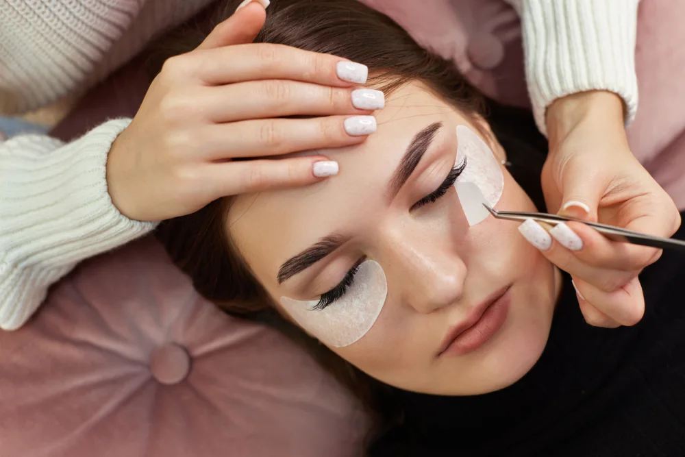 A lash technician carefully isolates and removes outgrown eyelash extensions using tweezers.