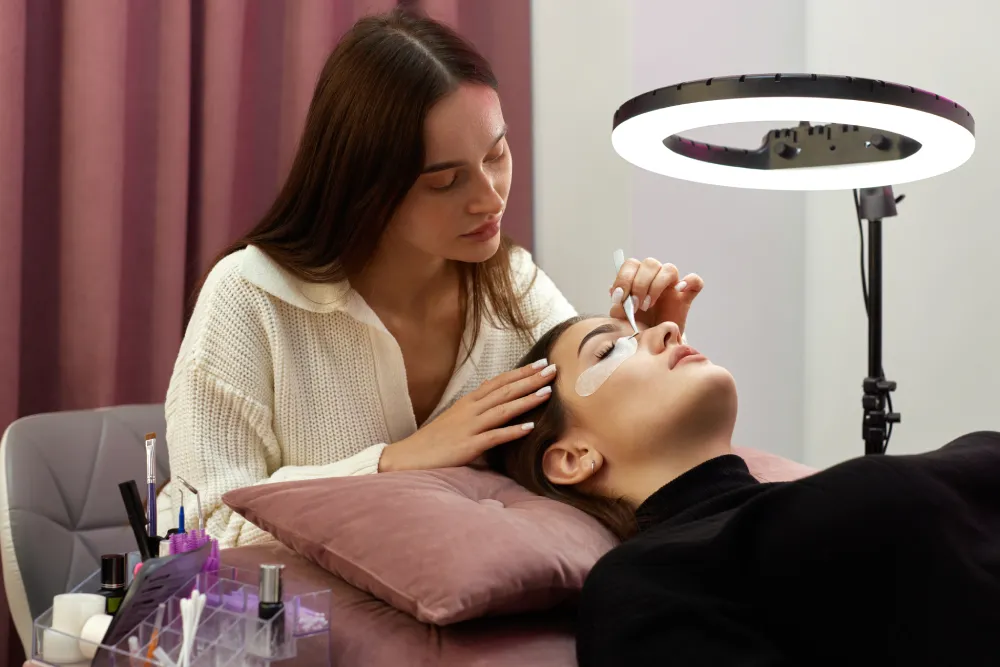 Close-up of a technician carefully applying lash remover cream/gel to the base of the eyelash extensions.