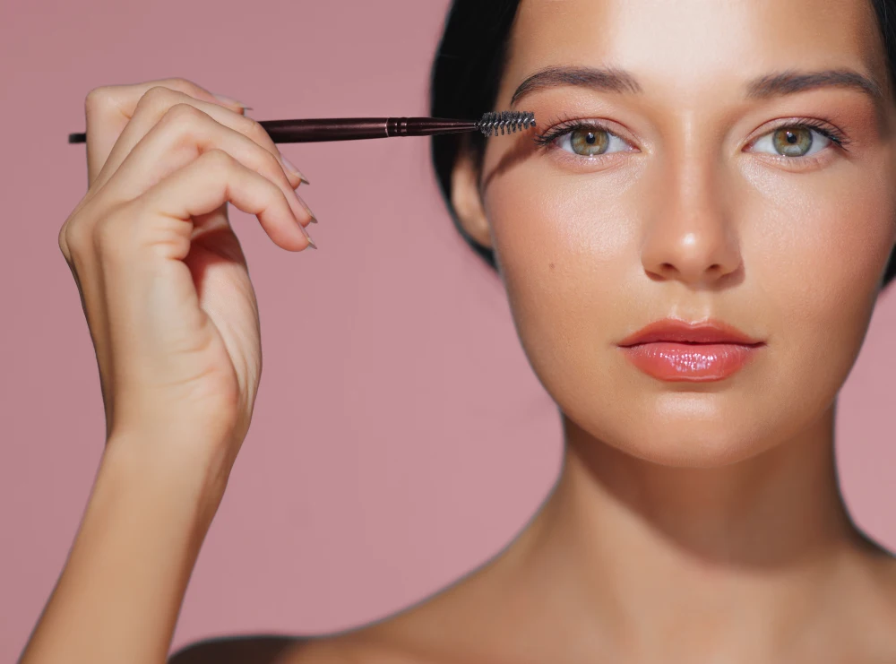A woman demonstrates how to apply a thin line of eyelash serum along the base of the lashes with a precise applicator brush.