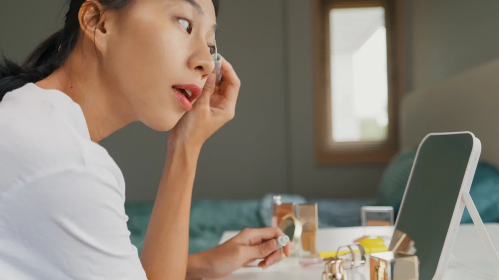 How to Correctly Use Eyelash Serums A woman looks in a mirror while correctly applying eyelash serum along her lash line, demonstrating the proper application technique.